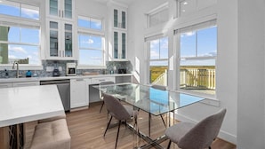 Una cocina moderna con armarios blancos, una mesa de comedor de vidrio y vistas al exterior.