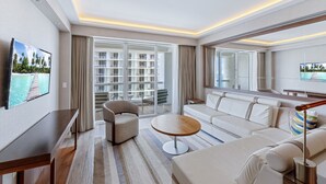 Une chambre d’hôtel moderne dotée d’une grande fenêtre, d’un canapé, d’un fauteuil, d’une petite table et d’un téléviseur fixé au mur.