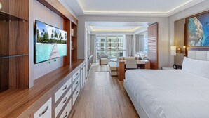 Une chambre d’hôtel moderne dotée d’un grand lit, d’une télévision, d’un bureau et d’un balcon offrant une vue sur l’océan.
