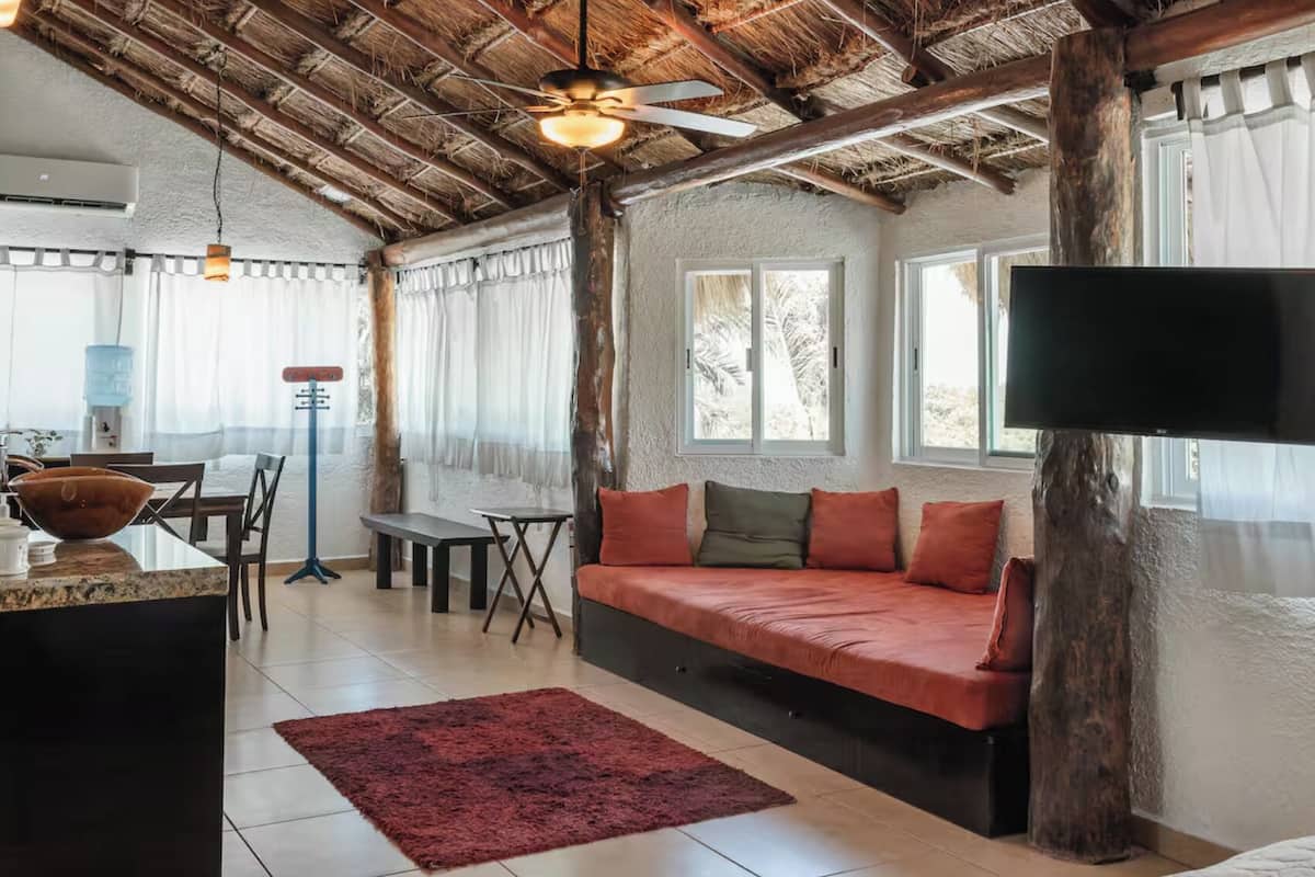 A cozy living area with a sofa, a TV, a dining table, and a large window.
