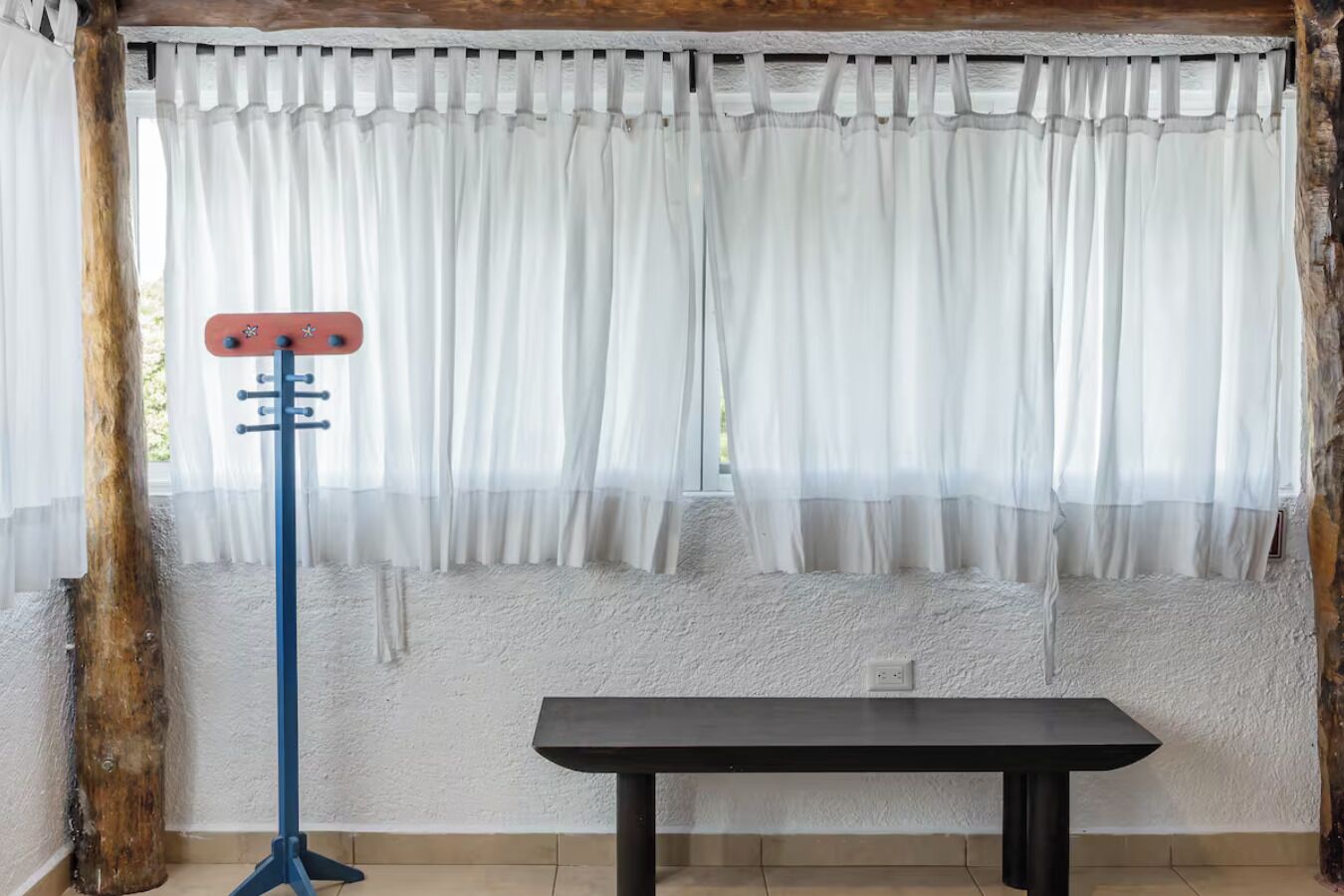 A room with a white textured wall, a wooden beam, a white curtain, and a black table.