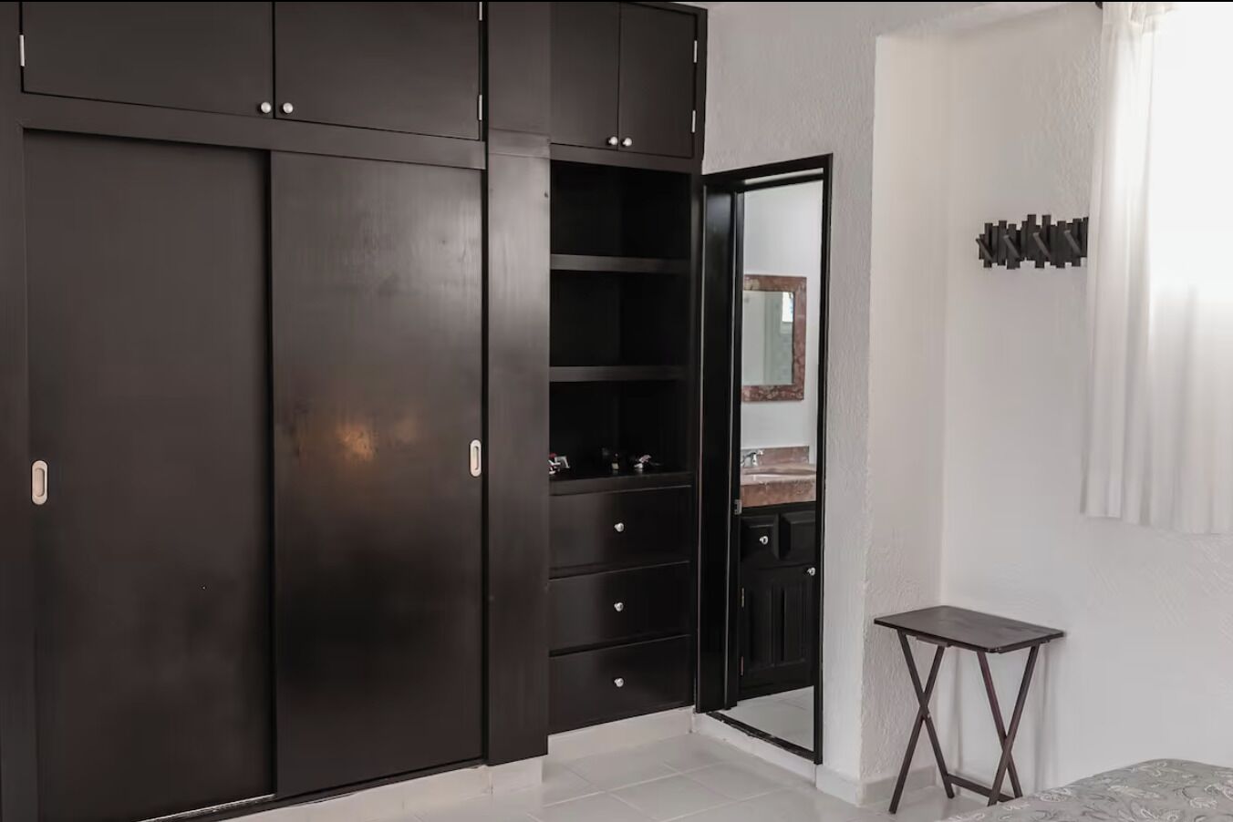 Un dormitorio con un armario oscuro, una mesita y un espejo.