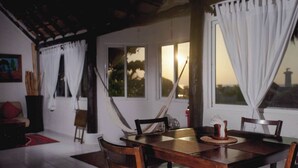 Un comedor con mesa y sillas de madera, cortinas blancas y vista al atardecer a través de las ventanas.