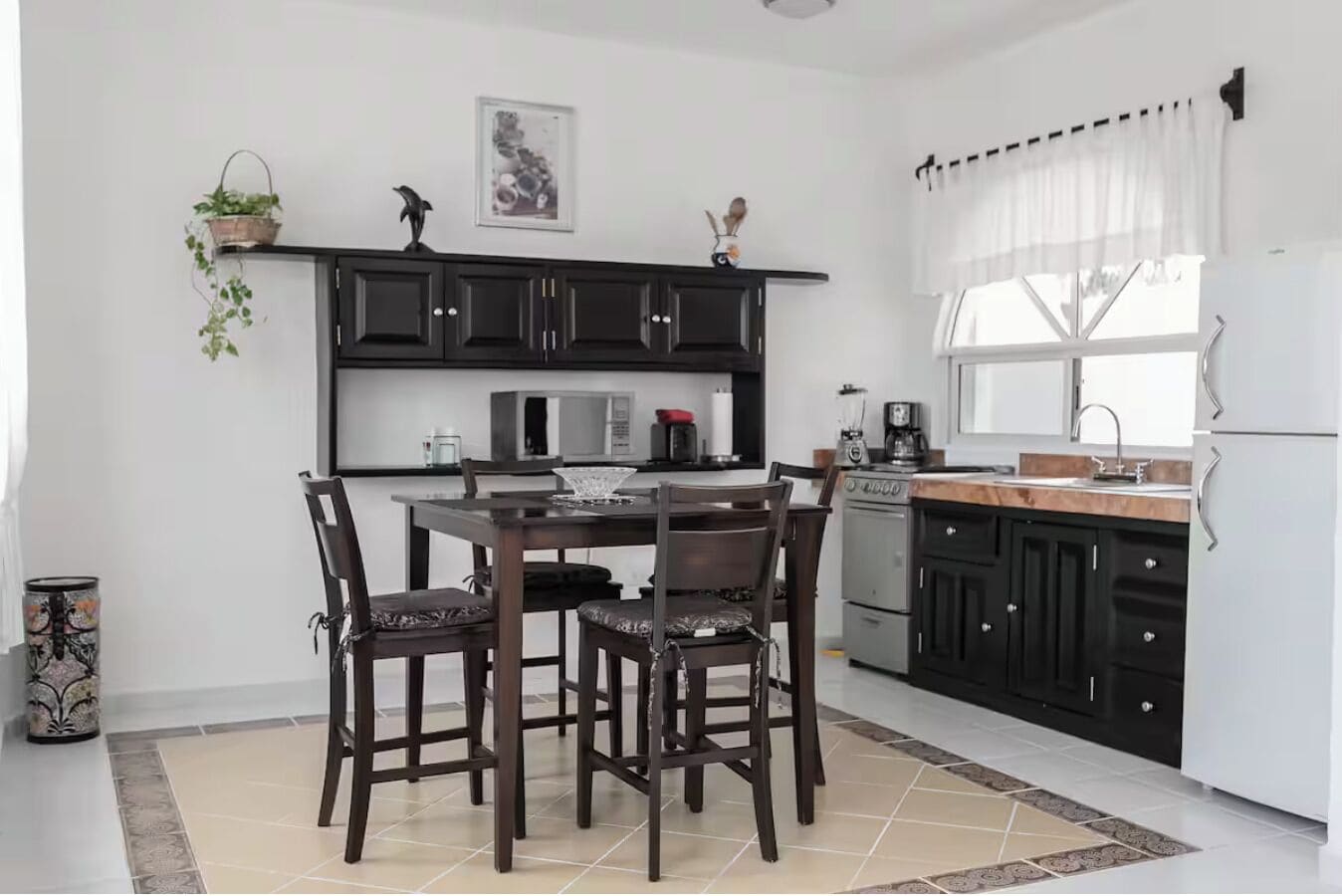 Une cuisine moderne avec des meubles de couleur sombre, un réfrigérateur blanc et un coin repas comprenant une table et des chaises.