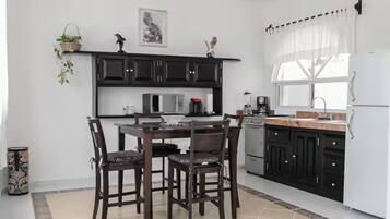 A modern kitchen with dark cabinets, a white refrigerator, and a dining area with a table and chairs.
