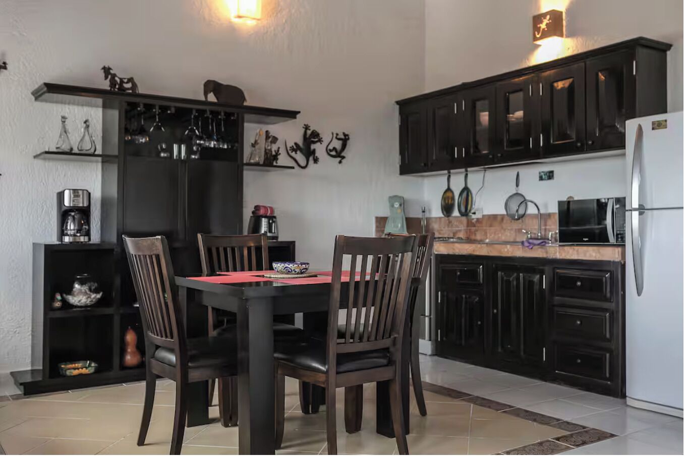 Een moderne keuken met donkere kastjes, een eettafel met stoelen en een inbouwkast met decoratieve objecten.