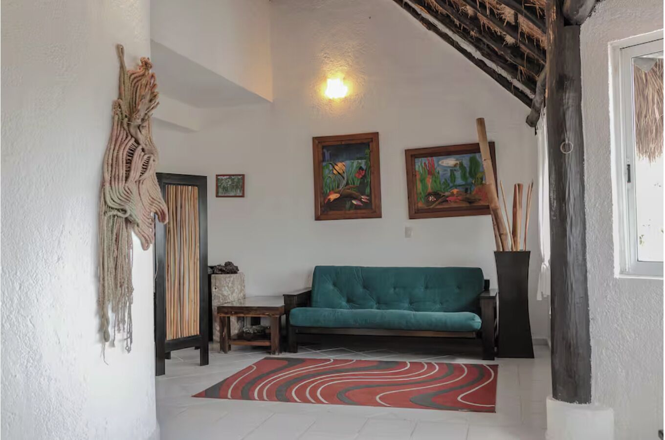 A living room with a teal sofa, a red and black rug, and two framed paintings on the wall.