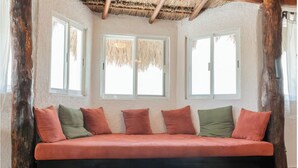 Habitación con sofá cama, ventanas amplias y techo de paja.