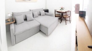 A modern living room with a grey sectional sofa, a small round table with chairs, a ceiling fan, and a flat-screen TV. - 9 Andar Com Vaga de Garagem Exclusiva (Rio de Janeiro)