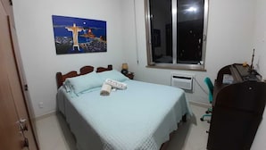 A bedroom with a bed, a window, a heater, and a chair. - 9 Andar Com Vaga de Garagem Exclusiva (Rio de Janeiro)