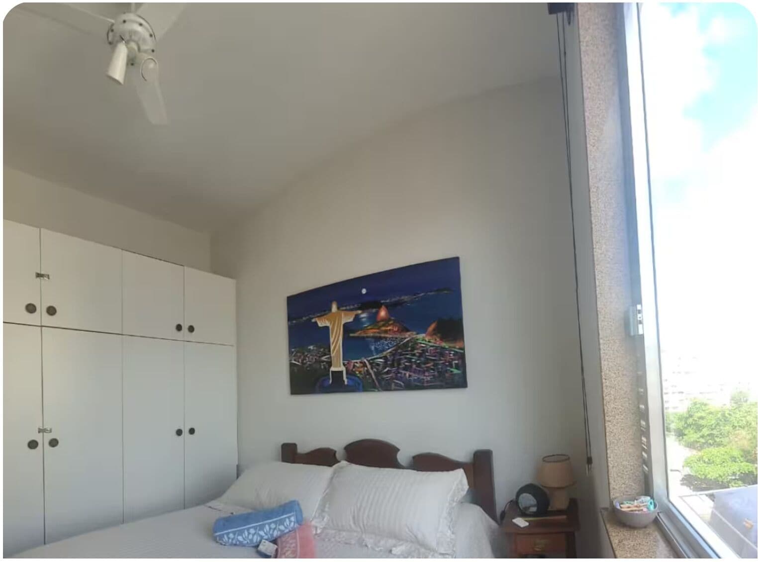 Une chambre à coucher avec un lit, une table de chevet, une fenêtre donnant sur un beau paysage et un ventilateur de plafond.