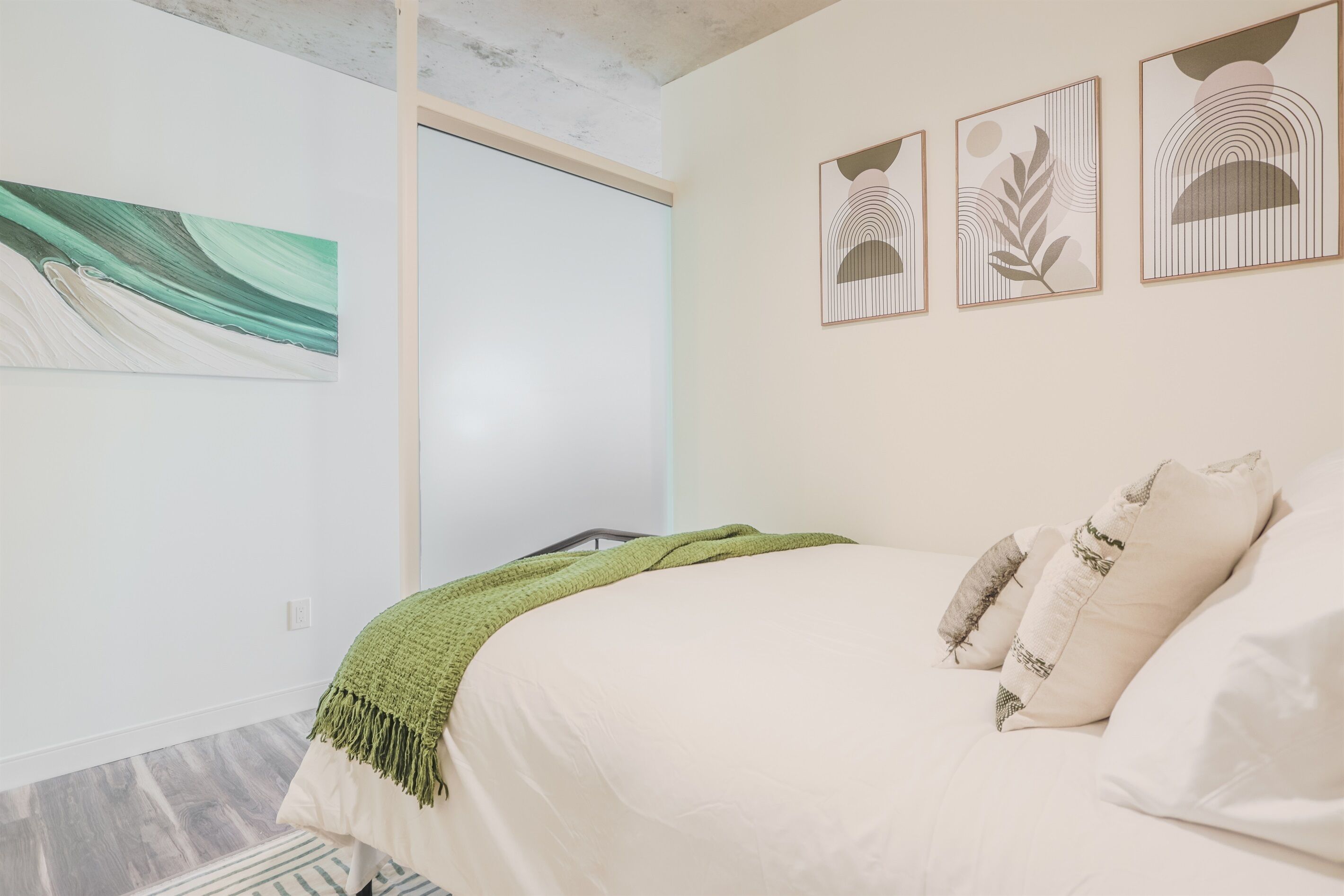 A bedroom with a bed, a green throw blanket, and three framed artworks on the wall.