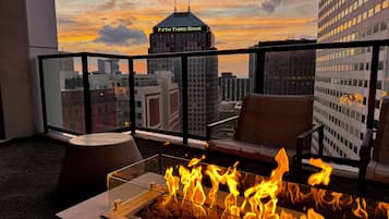 A balcony with a glass railing, a fire feature, and a view of a cityscape including a building labeled 'Fifth Third Bank.'