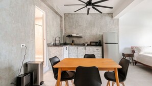 Une cuisine moderne avec un coin repas, un ventilateur de plafond et un lit dans une pièce dont un mur est en béton et le sol est blanc.