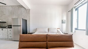 Une chambre moderne avec un lit, un canapé au premier plan, un coin cuisine et une grande fenêtre.