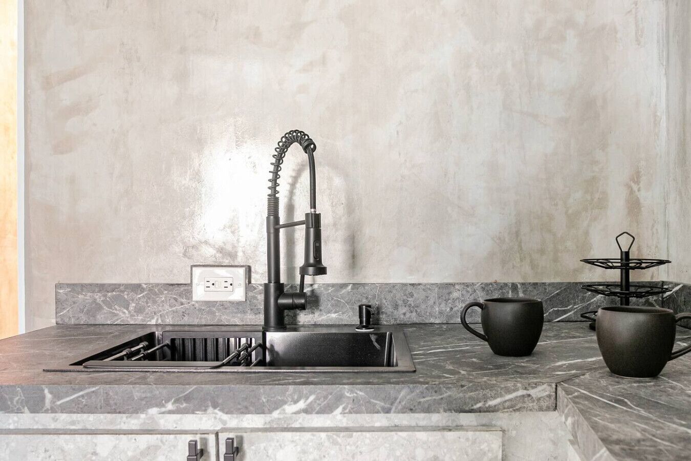 Una cocina moderna con un grifo negro elegante, una encimera de mármol y una taza y una olla negras sobre la encimera.