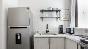A modern kitchen with a stainless steel refrigerator, a sink, a microwave, and a coffee maker. There are shelves above the sink holding dishes and glasses. - Modern 2 Bed Room Suite in Art District (San Juan)