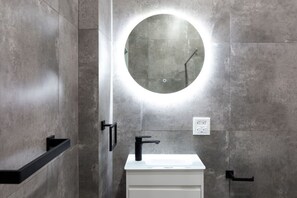 A modern bathroom with a round mirror, a white sink, and a black faucet. - Cozy 2 Bed Room in Art District (San Juan)