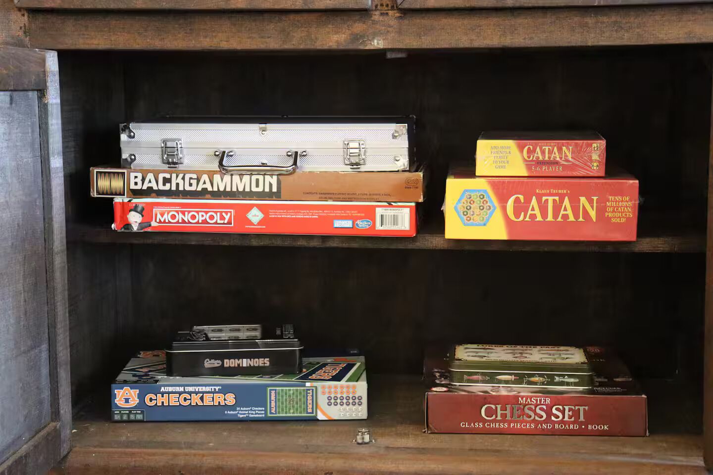 Una estantería de madera con varios juegos de mesa, incluyendo Backgammon, Monopoly, Catan y un juego de ajedrez.