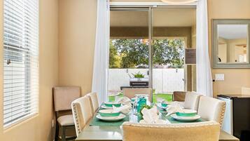 A dining area with a table set for four, a chair, a grill, and a view of the backyard.