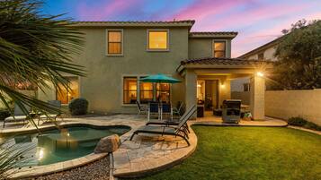 A two-story house with a swimming pool, a patio with lounge chairs, and a covered outdoor area.