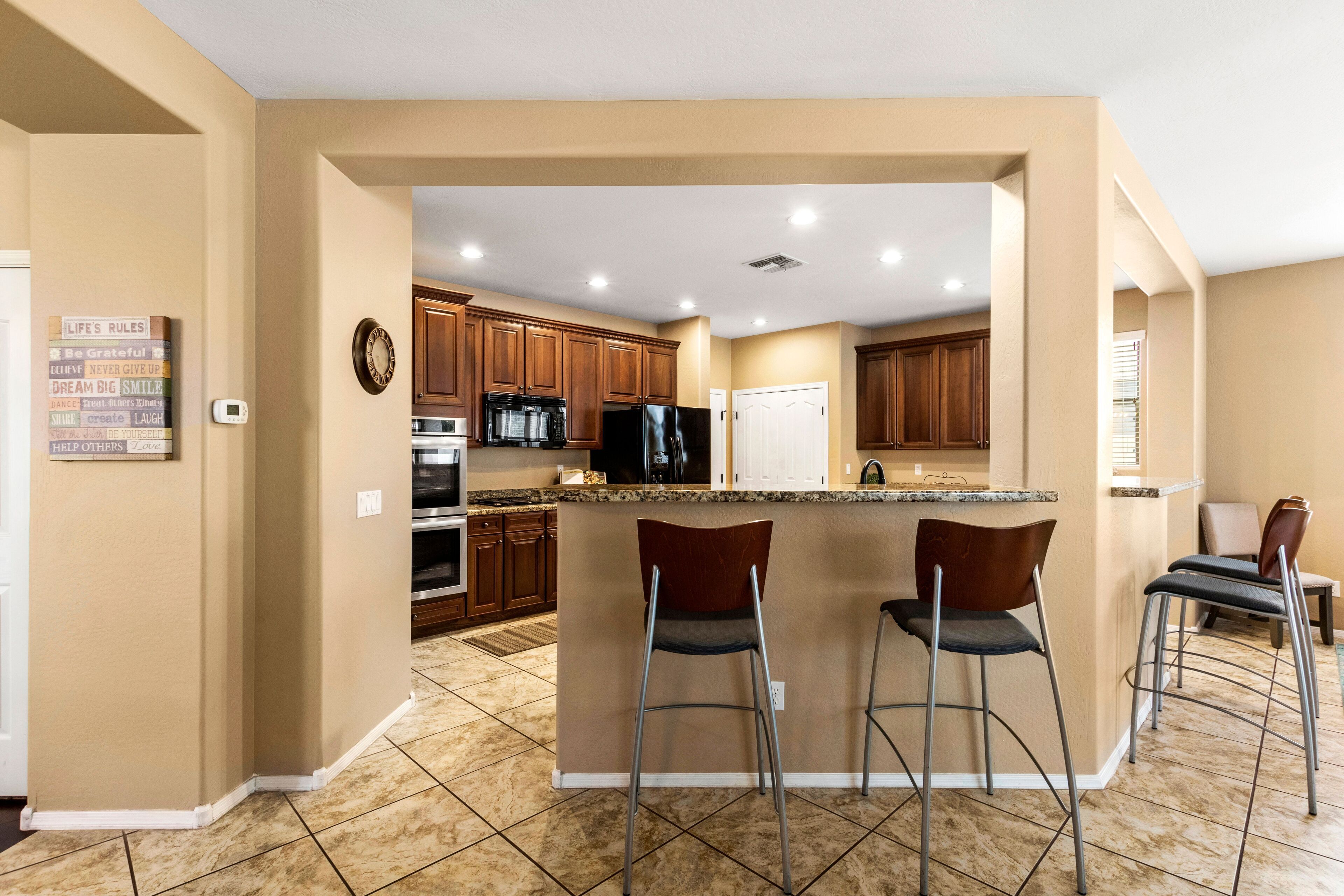 A modern kitchen with a central island, bar stools, wooden cabinets, and a clock on the wall.