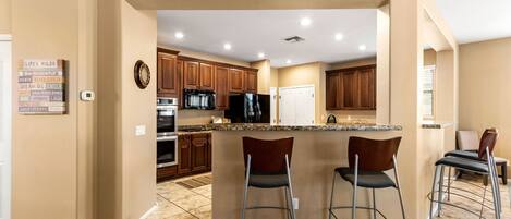 A modern kitchen with a central island, bar stools, wooden cabinets, and a clock on the wall.