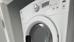 Une machine à laver et un sèche-linge superposés, dans une pièce dotée d’une porte et de murs aux couleurs claires.