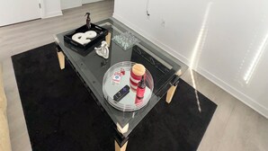 Un salon moderne avec une table basse en verre, un téléviseur à écran plat fixé au mur et une porte visible au fond.