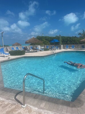 A swimming pool with clear blue water, lounge chairs, and a thatched umbrella.
