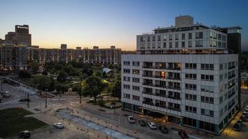 A multi-story hotel with a modern design, featuring a central courtyard and a parking area with several cars.