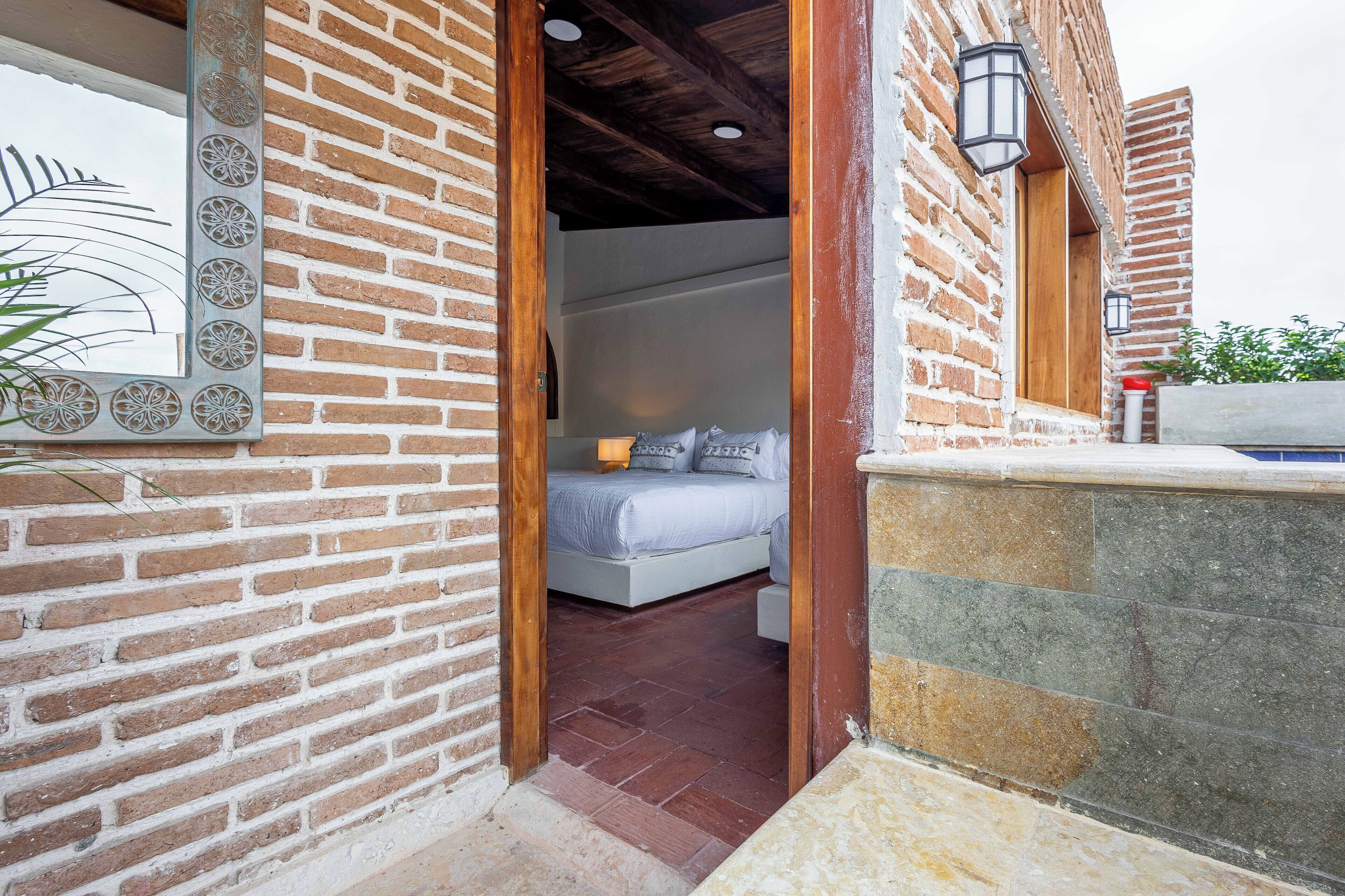 Un dormitorio con pared de ladrillo, techo de madera y cama con ropa blanca.