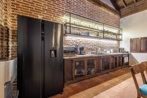 A kitchen with a brick wall, a black refrigerator, a stainless steel sink, and a wooden chair.