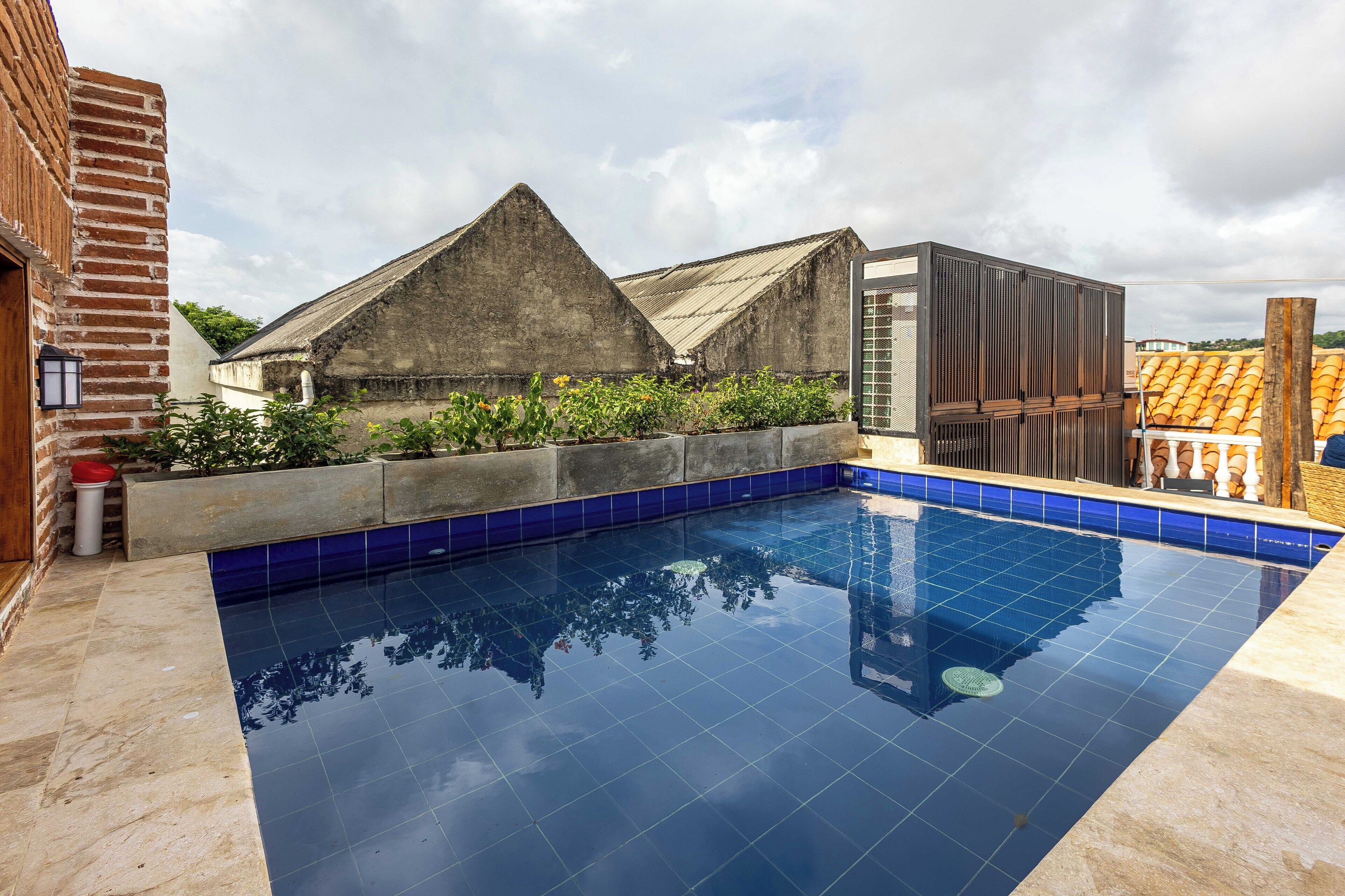 Une piscine aux carreaux bleus, un bâtiment en briques et une structure moderne dotée d’un toit en pente.