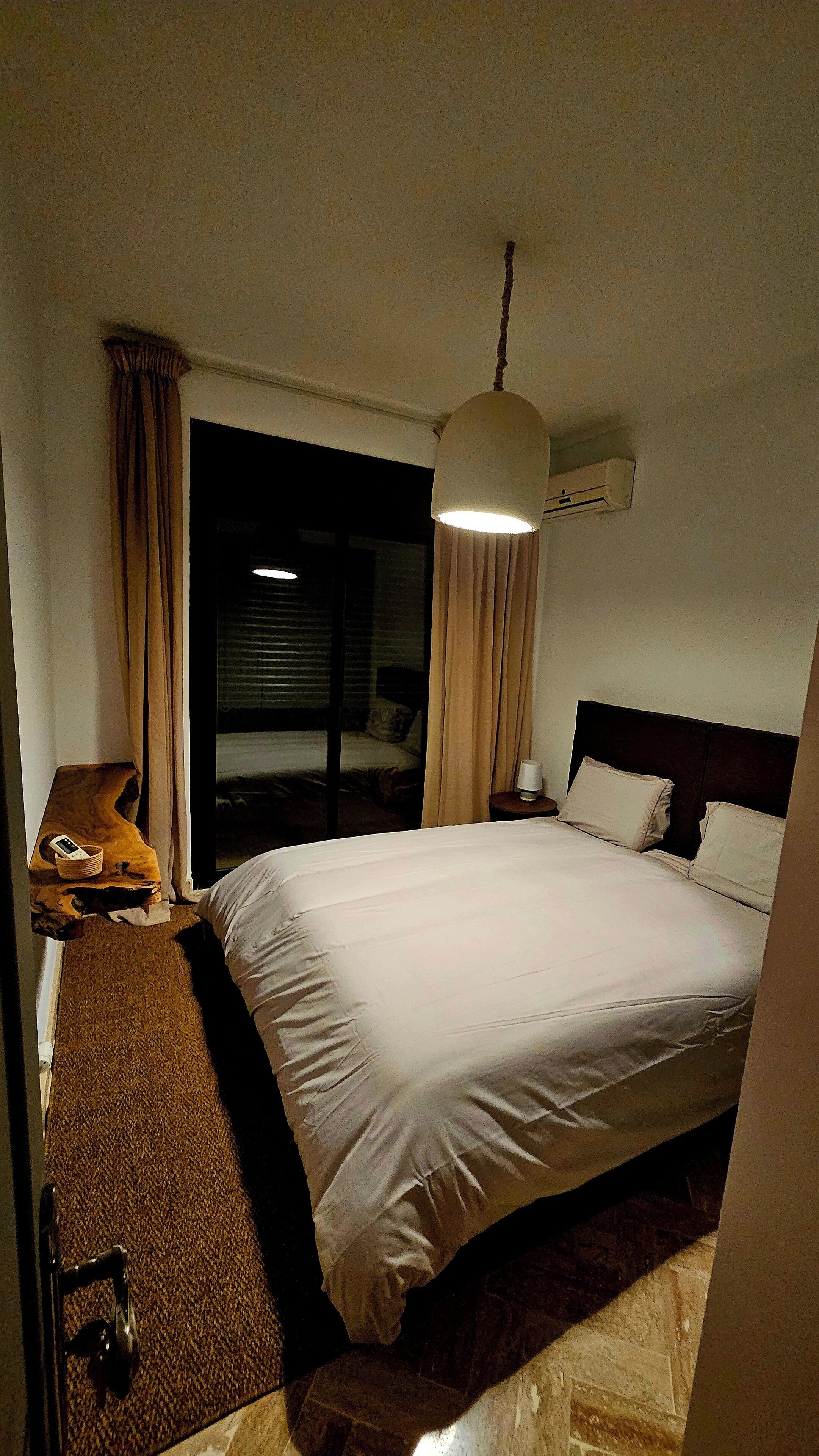A hotel room with a large bed, a bedside table, a lamp, and a window with curtains.