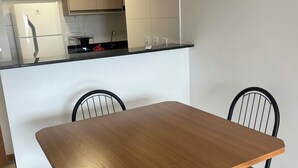 Ett modernt kök med vita skåp, en svart bänkskiva och en inbyggd ugn. Runt ett träbord står fyra svarta stolar med bruna dynor.