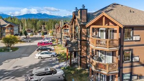 A multi-story lodge with a wooden exterior, balconies, and a parking area with several cars. - Bighorn Manor | Central | Wood Fireplace | Views (Radium Hot Springs)