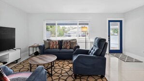Ein modernes Wohnzimmer mit einer Couch, einem Sessel, einem Couchtisch, einem Fernseher und einem gemusterten Teppich.