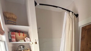 Une salle de bain avec une douche, une porte blanche, un plancher en bois et un tapis à motifs bleus.