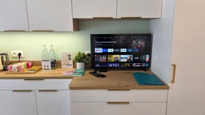 Eine moderne Küche mit integriertem Fernseher, der eine Streaming-Dienstanwendung anzeigt, einem Wasserkocher und verschiedenen Küchenutensilien auf der Arbeitsplatte.