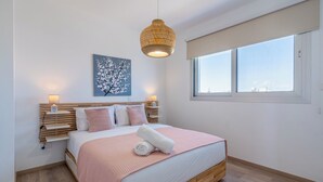 Un dormitori amb llit, tauletes de nit, una finestra i una obra d'art penjada a la paret.