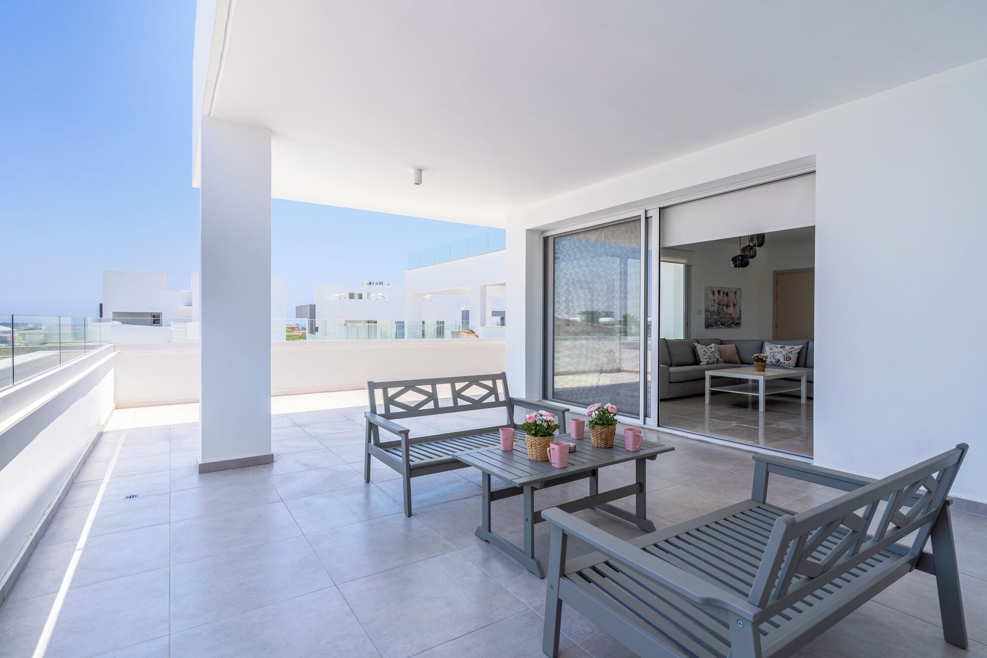 A balcony with a table and benches, a sofa, and a sliding glass door leading to a living area.