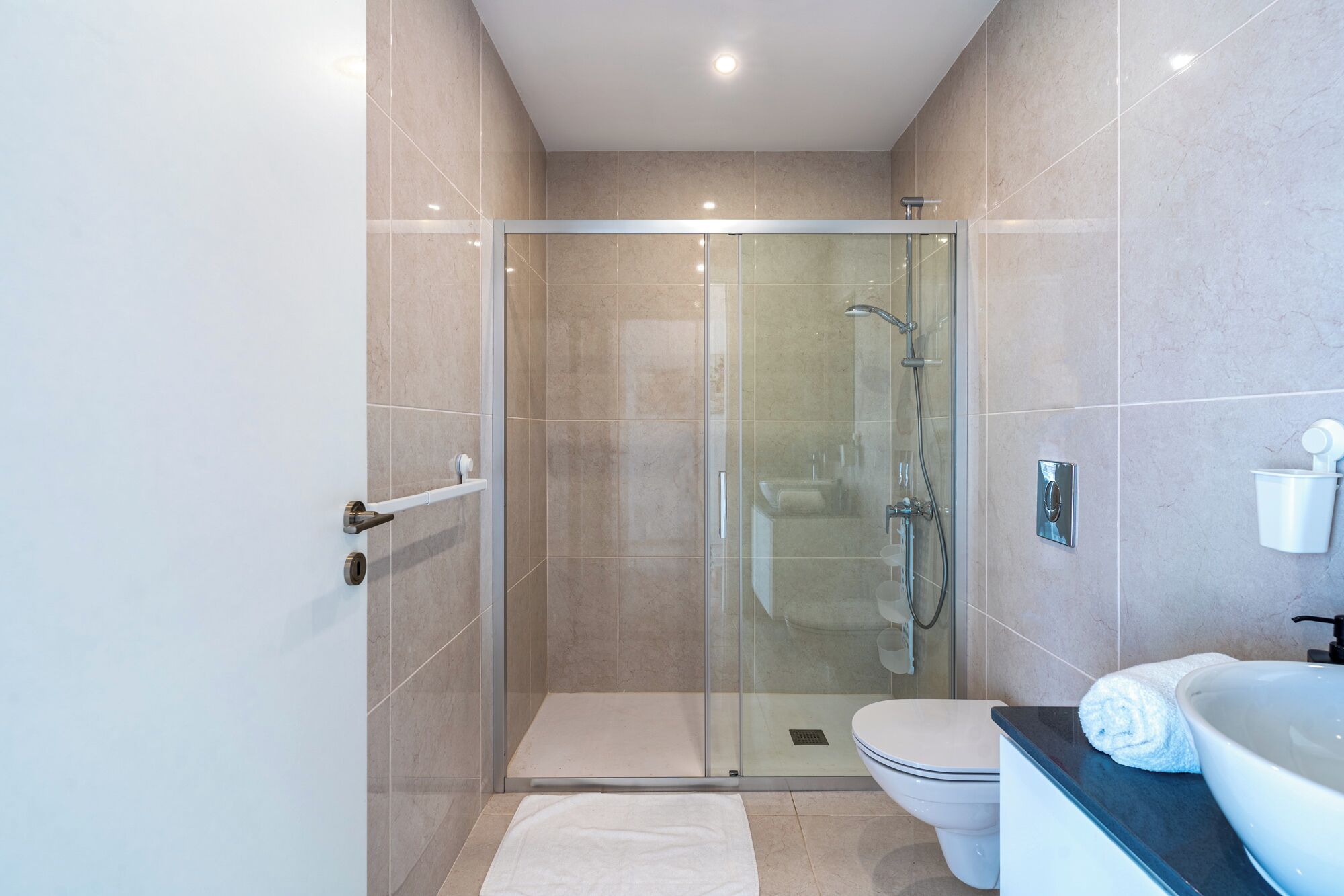 A modern bathroom with a glass-enclosed shower, a toilet, and a sink with a towel.