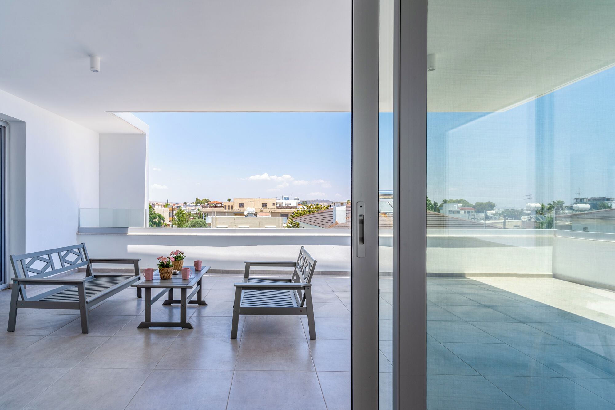 A modern balcony with two metal-framed chairs and a small table, overlooking a cityscape.