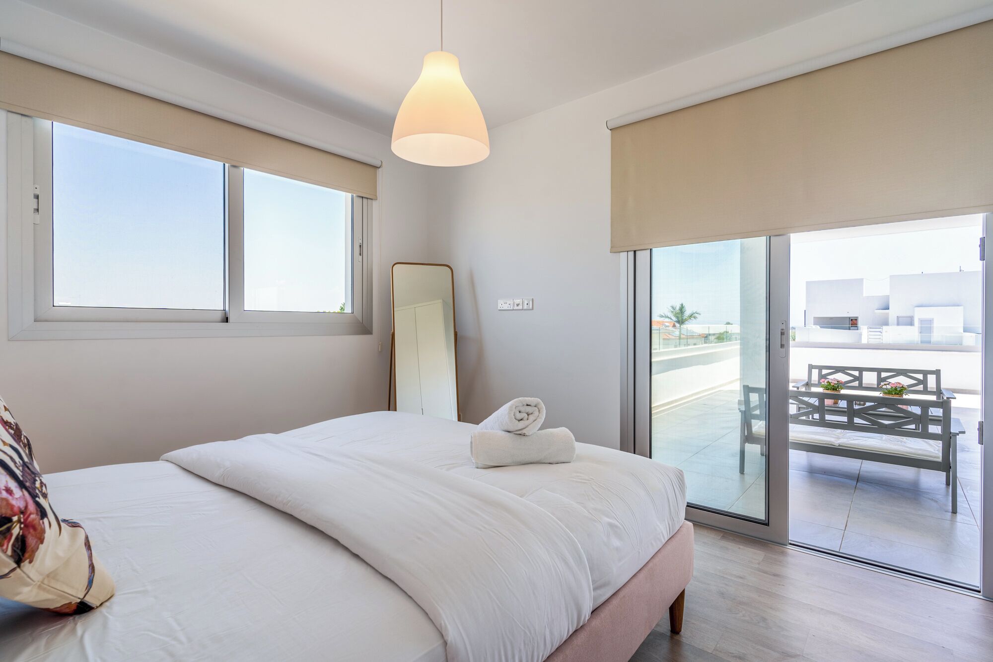 Un dormitorio con una cama grande, una mesita de noche, una lámpara colgante y vistas al balcón exterior.