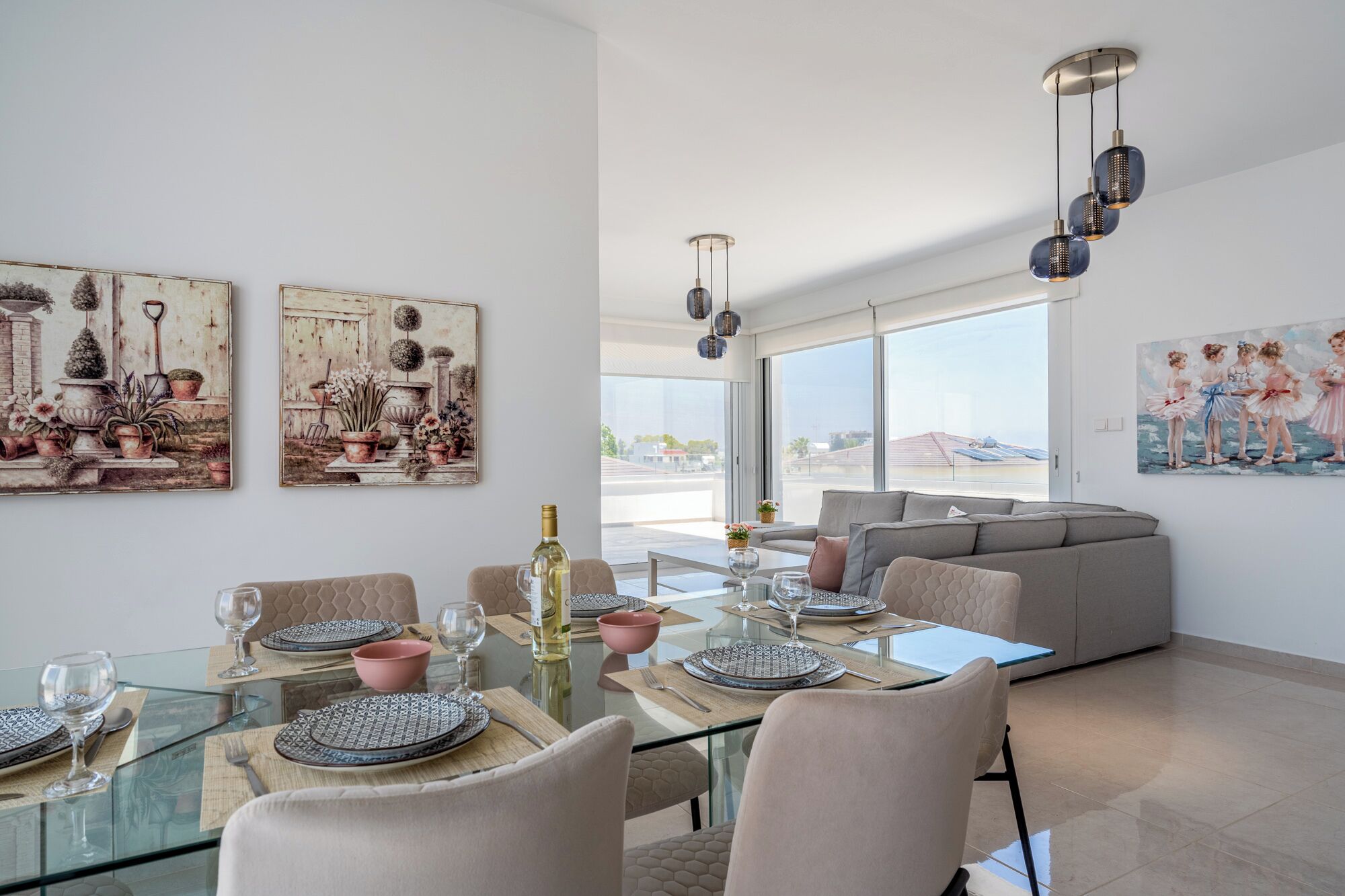 A modern dining area with glass tables, grey upholstered chairs, and artwork on the walls.