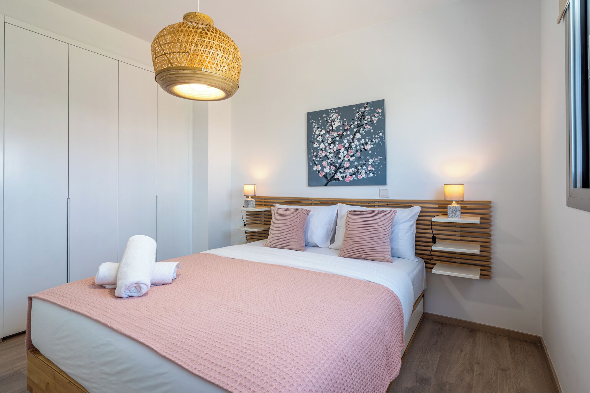 A bedroom with a bed, bedside lamps, a wall-mounted artwork, and a hanging light fixture.