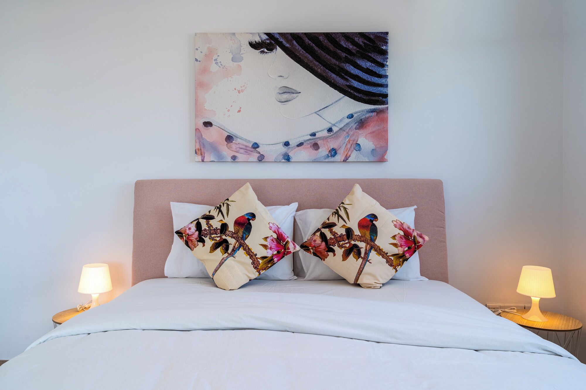 Ein ordentlich bezogenes Bett mit weißer Bettwäsche und zwei dekorativen Kissen mit bunten Vögeln und Blumen.