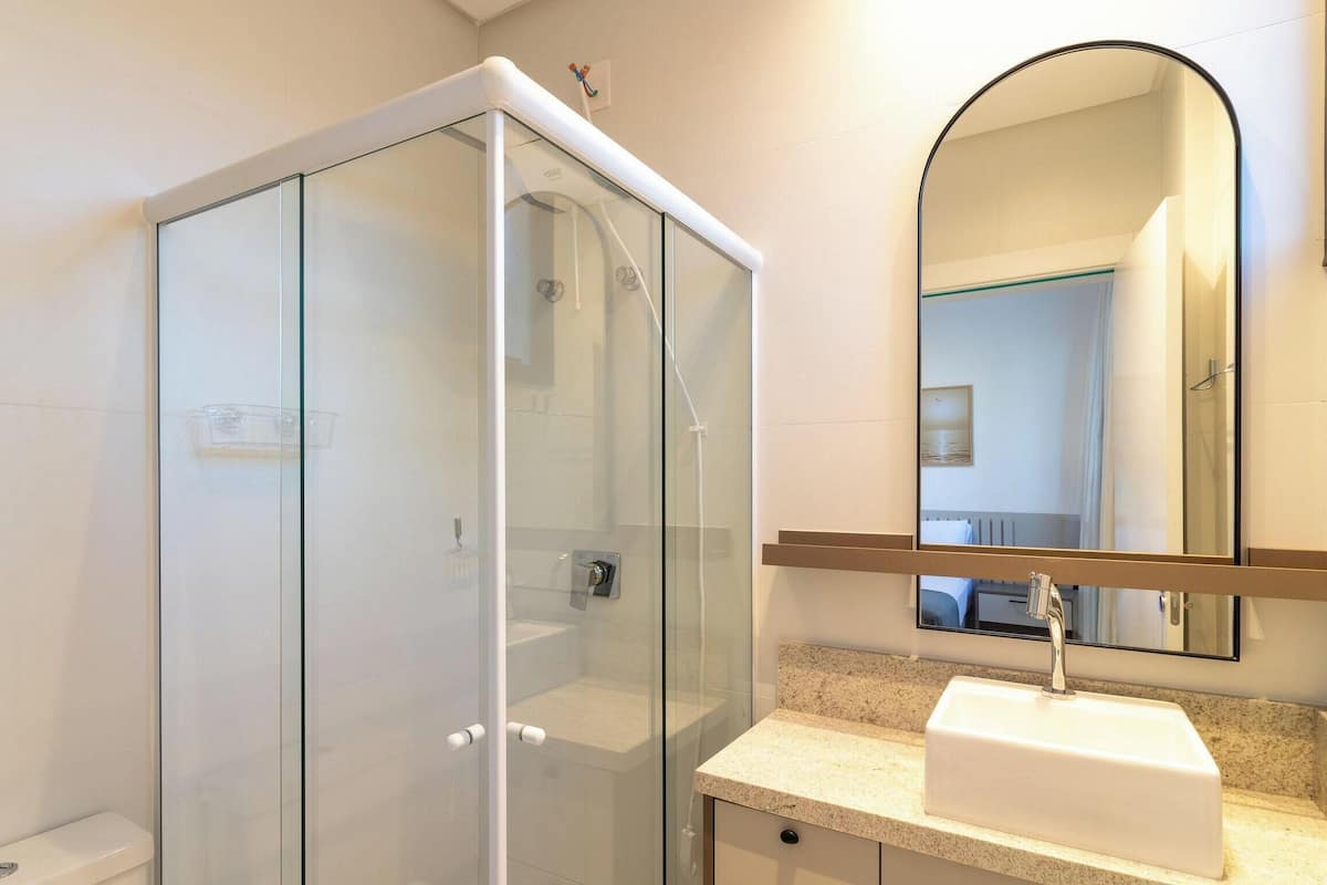 A modern bathroom with a glass-enclosed shower, a white sink, and a large mirror.