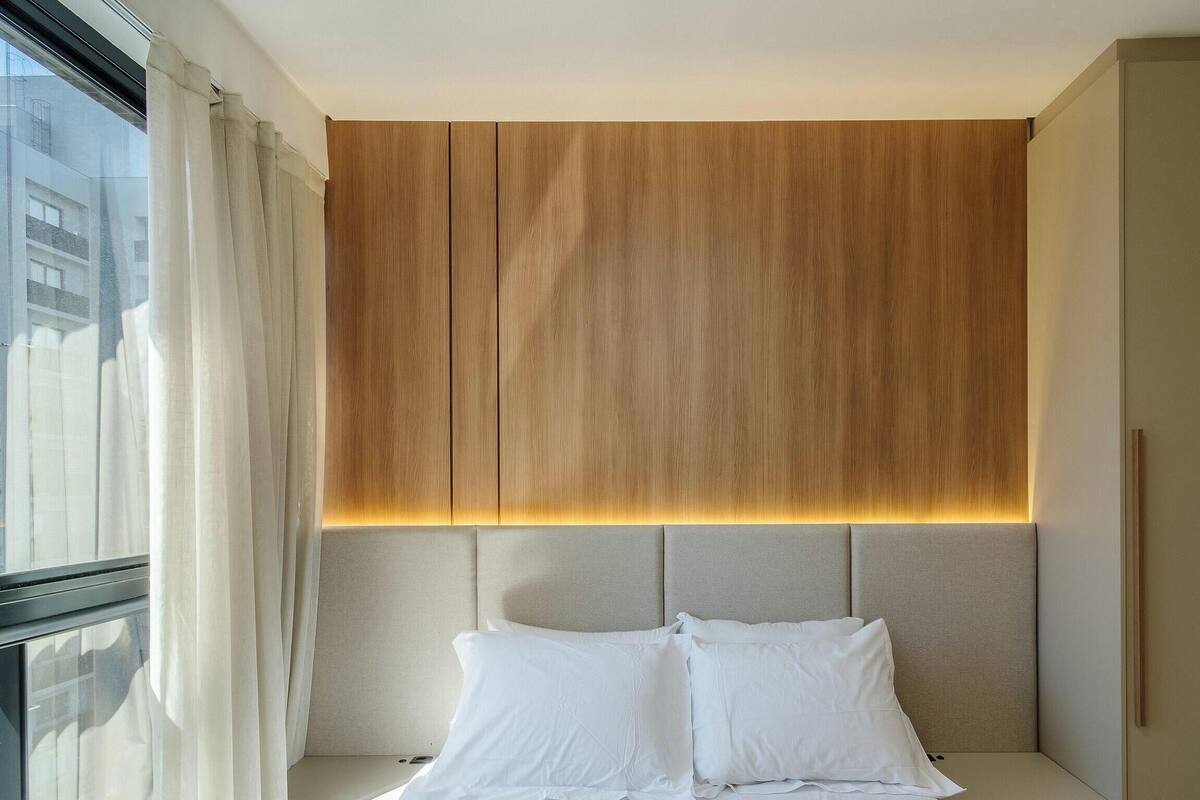 A modern hotel room with a large bed, a wooden headboard, and a view of the city through the window.